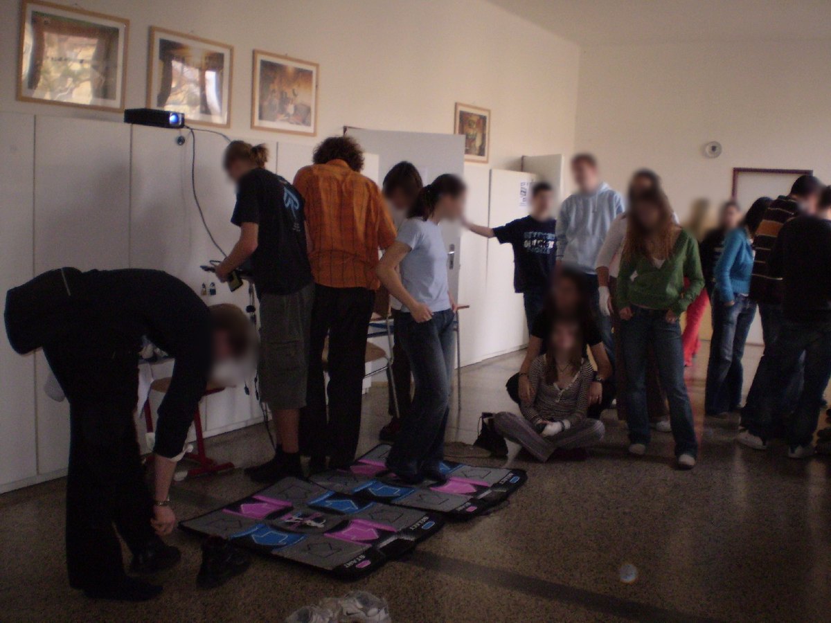 High school students gather around dance pads in a classroom with a projector, in Slovakia